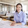 Female Asian architect smiling to camera in open plan office