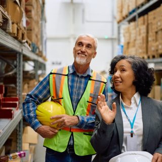 Happy businesswoman and warehouse foreman communicating at storage compartment.